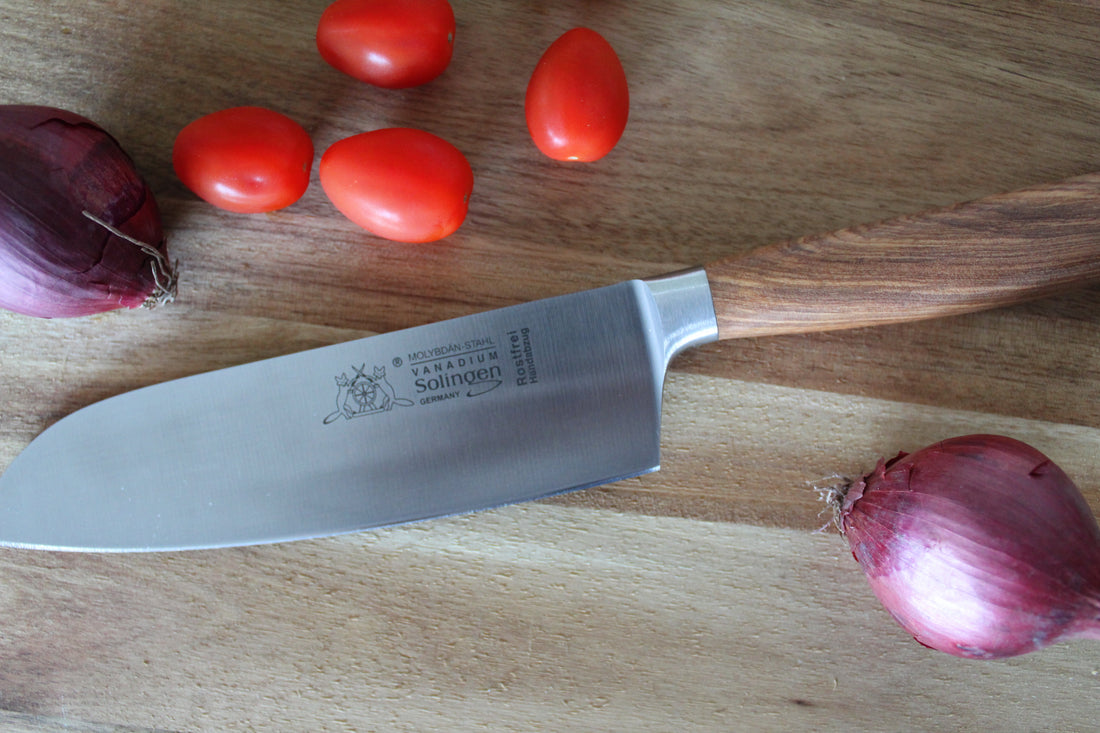 Schönes geschmiedetes Santokumesser auf einem Holzbrett mit Tomaten und Zwiebeln zur Deko